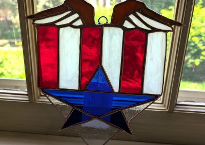 A stained glass shield with eagle wings strips and a star in Red White and Blue | Copper & Light Studio