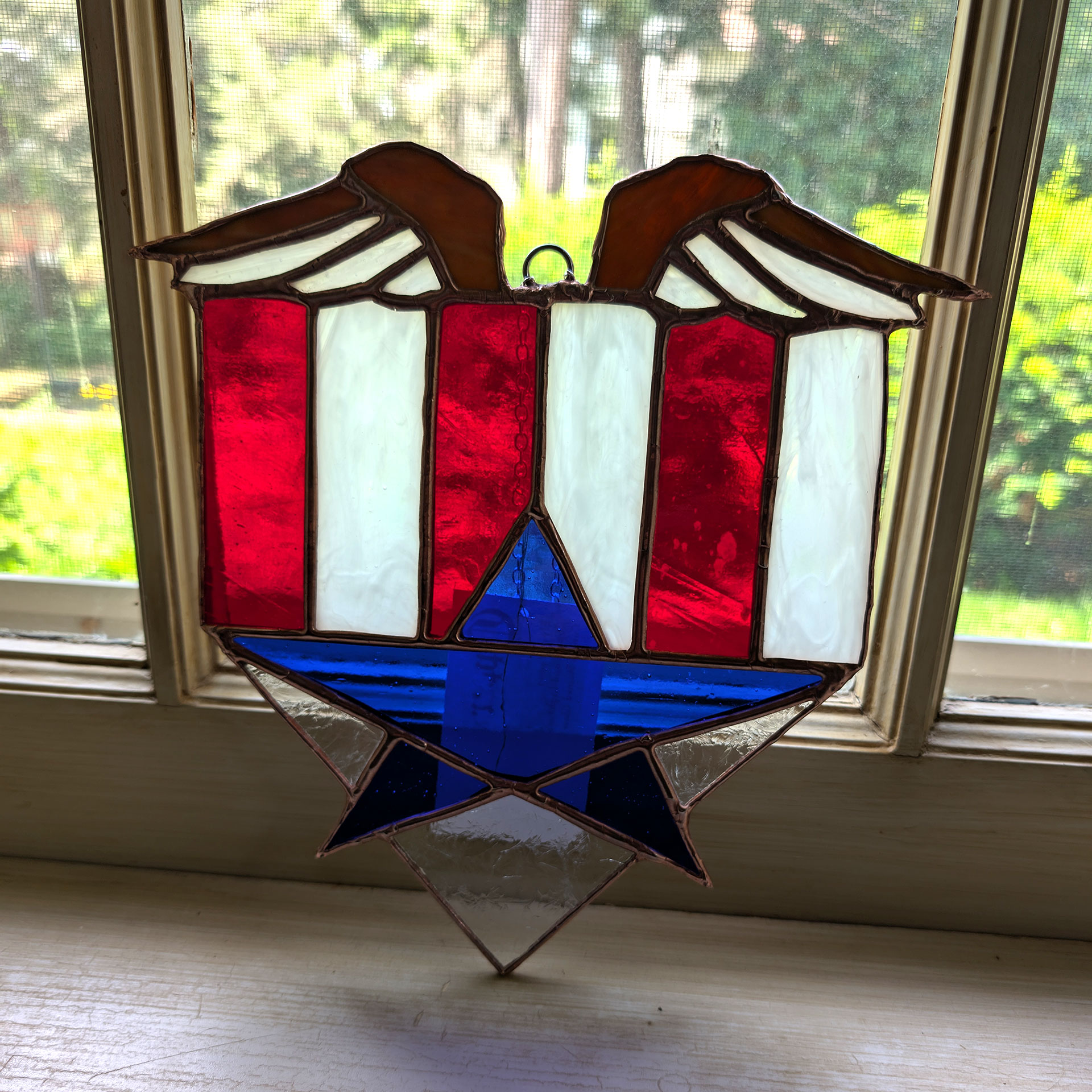 A stained glass shield with eagle wings strips and a star in Red White and Blue | Copper & Light Studio